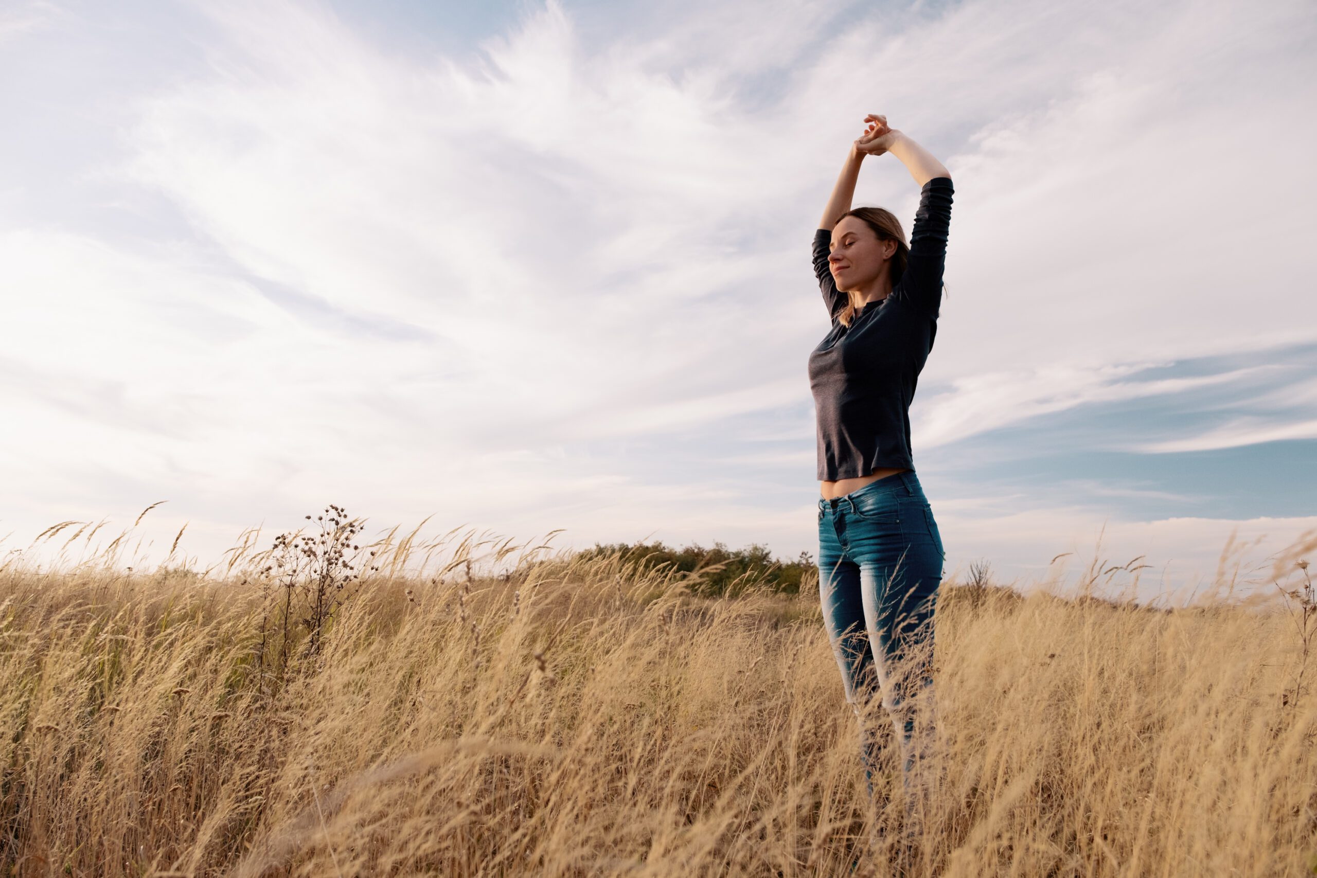 Young woman enjoying nature and freedom in a golden field under the blue sky