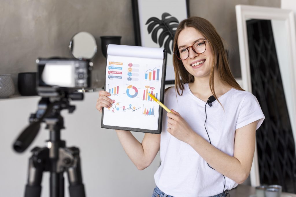 young-blogger-recording-with-professional-camera-holding-clipboard-with-graphics-1024x683